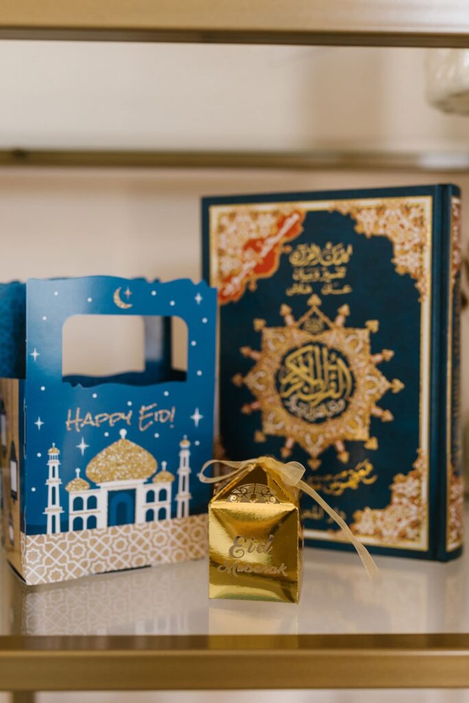 Two golden gift boxes, one gold, the other blue with the words "Happy Eid" in the office used as decoration next to a Quran.